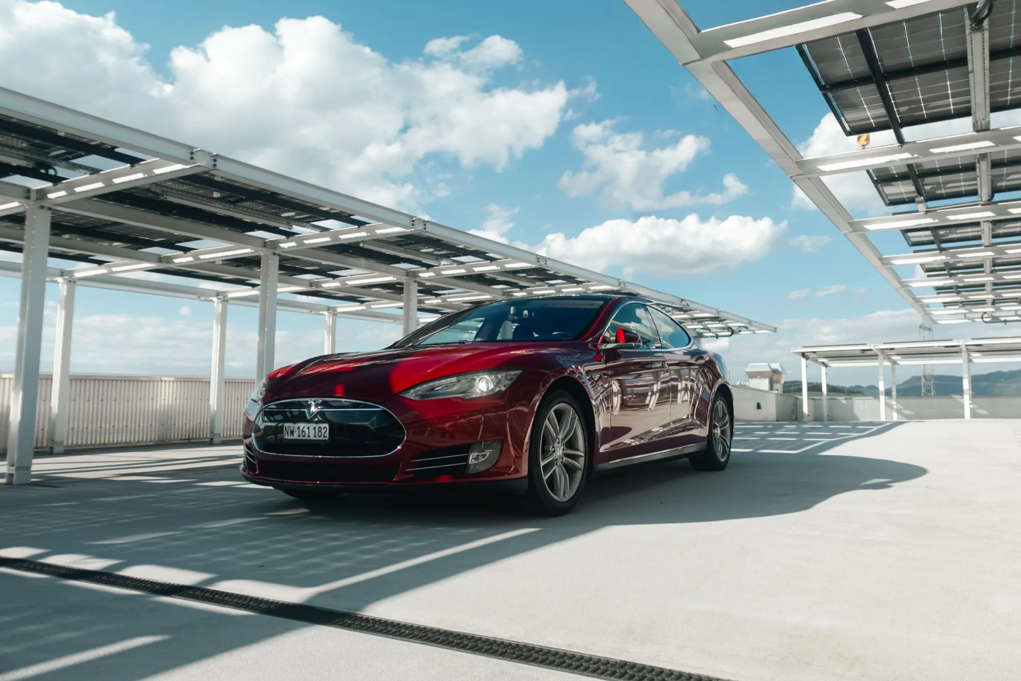 Roter Tesla Model S schräg von vorne auf einem Parkdeck unter einer Solarüberdachung